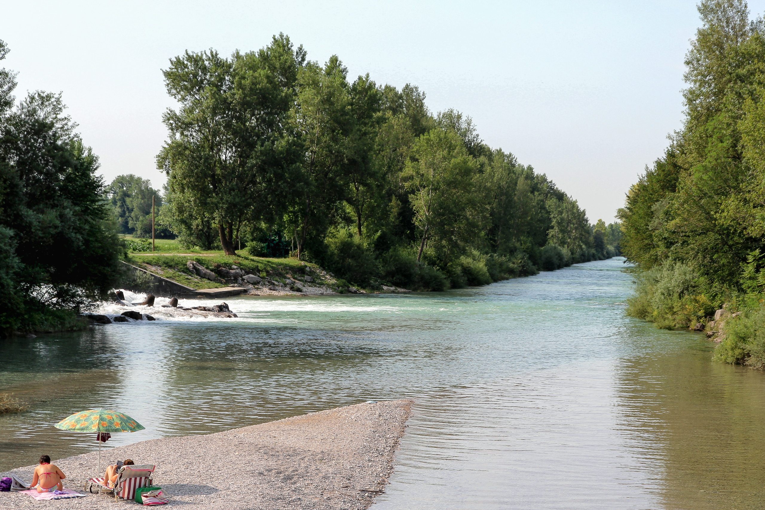 Früh am Wasser: ein Sonnenschirm auf der Kiesbank, dahinter das Wehr